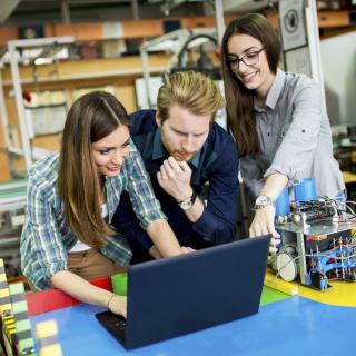 Drei Schülerinnen und Schüler arbeiten in einer Robotikwerkstatt.